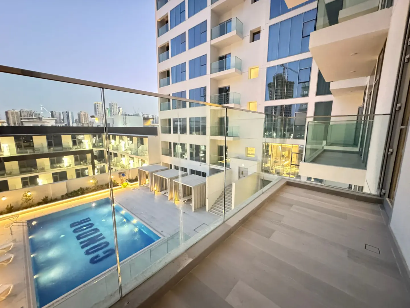View from a balcony overlooking a pool with "Condor" written in it, cabanas, and a modern building.