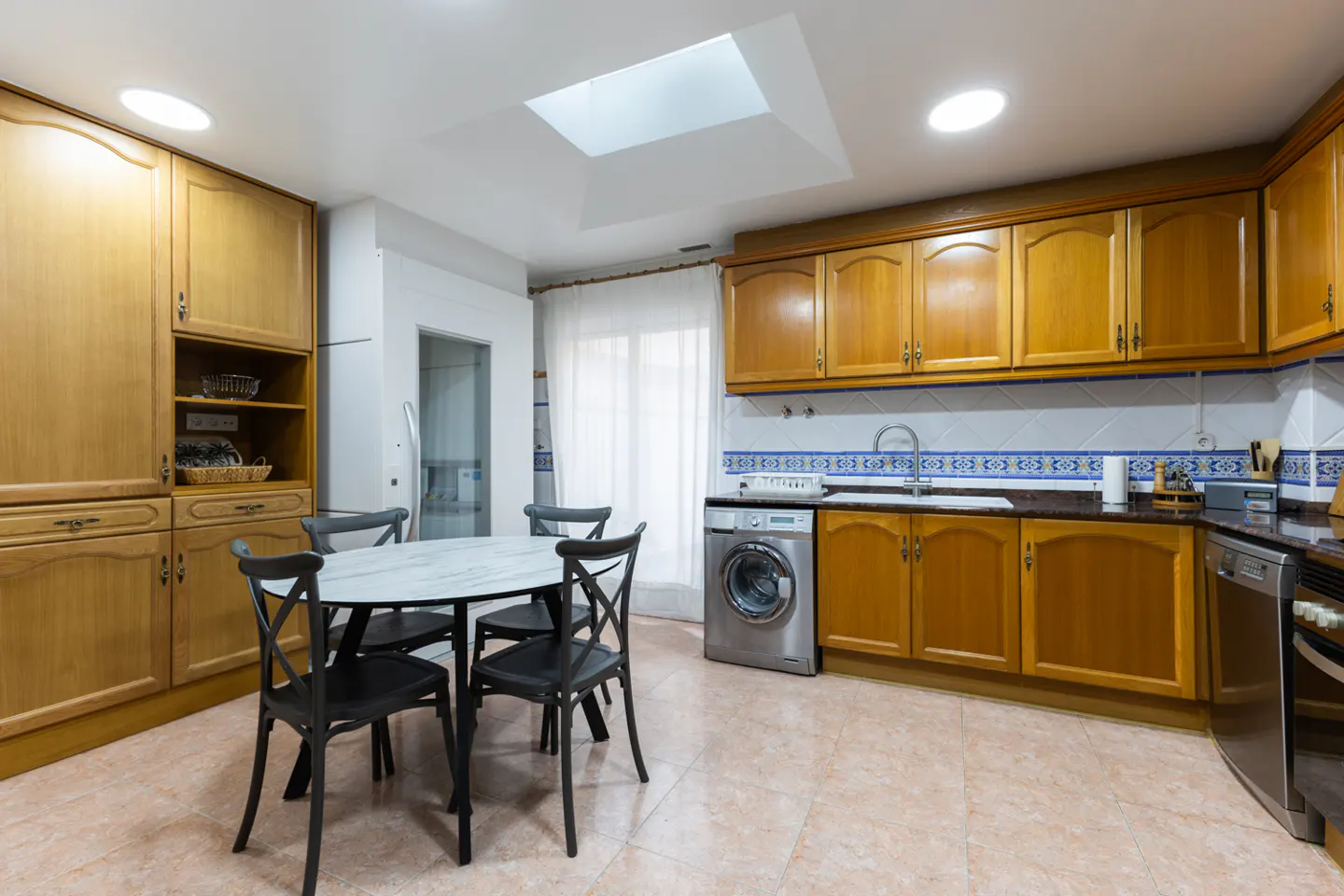 Kitchen with wooden cabinets, marble-topped dining table, four black chairs, stainless appliances, and a skylight.