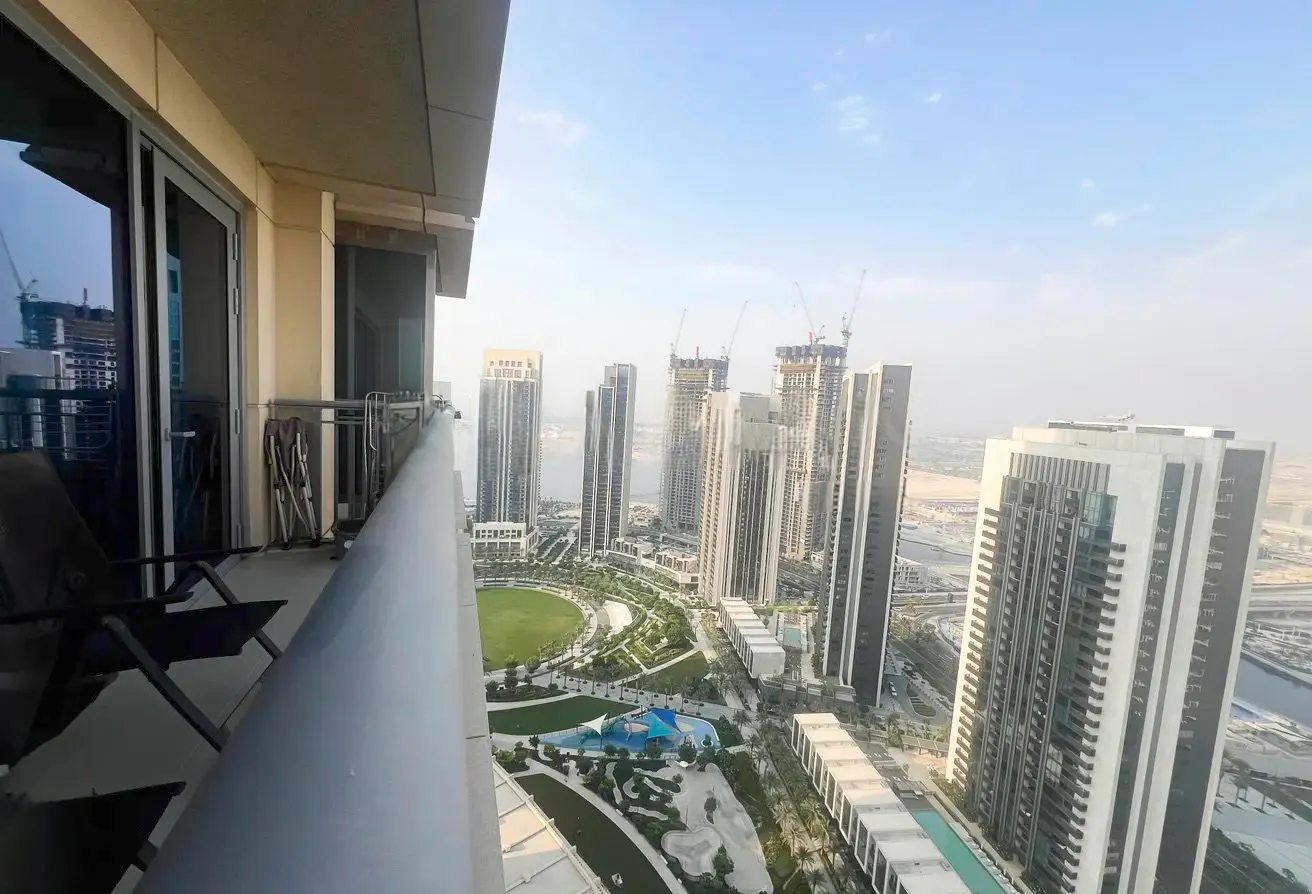View from a high-rise balcony with chairs overlooking a park and city skyline with tall buildings.