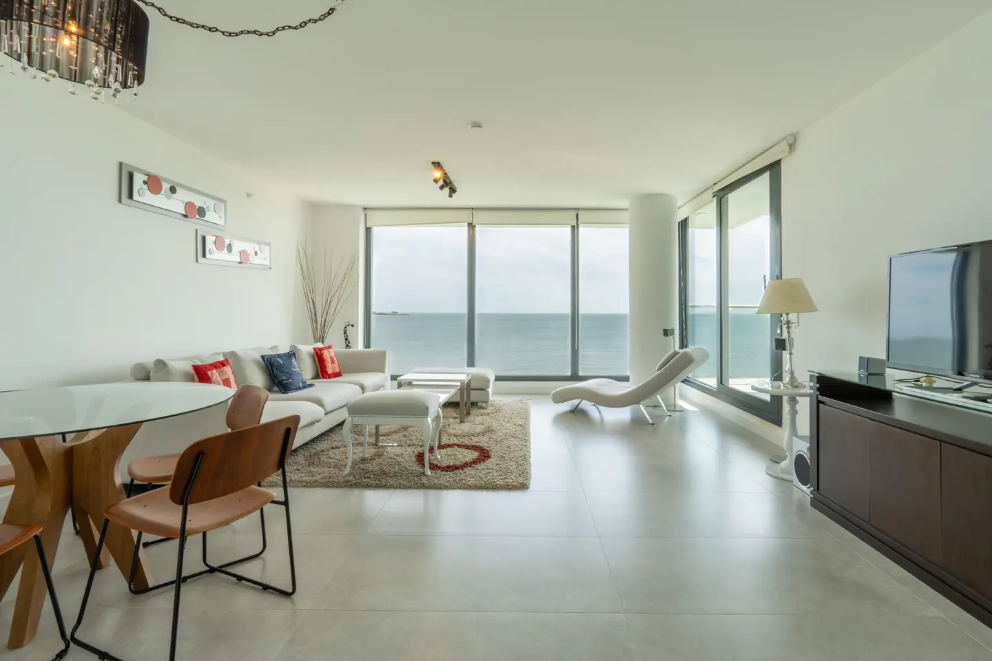 Modern living room with white sofa, dining area, and floor-to-ceiling windows overlooking the ocean.