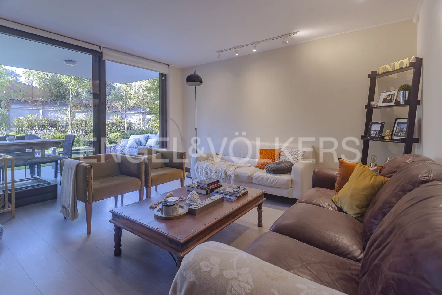 Living room with brown leather sofa, white sofa, wooden coffee table, and two armchairs. Sliding glass doors lead to a patio.