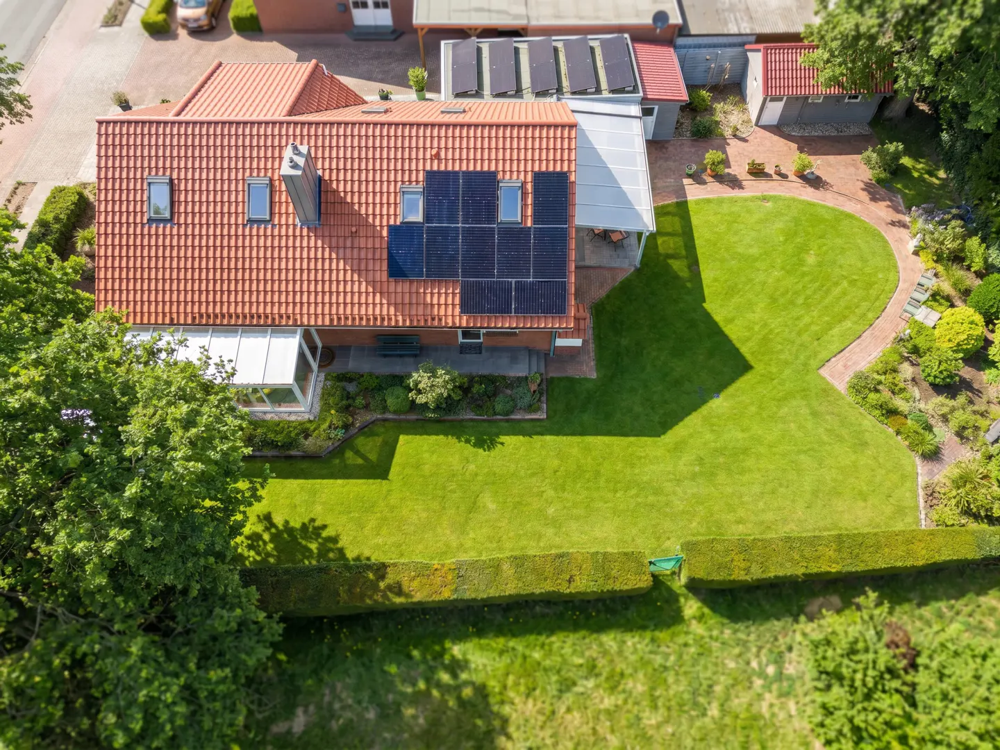 Aerial view of a house with a red tile roof, solar panels, a sunroom, and a green lawn with a brick path.