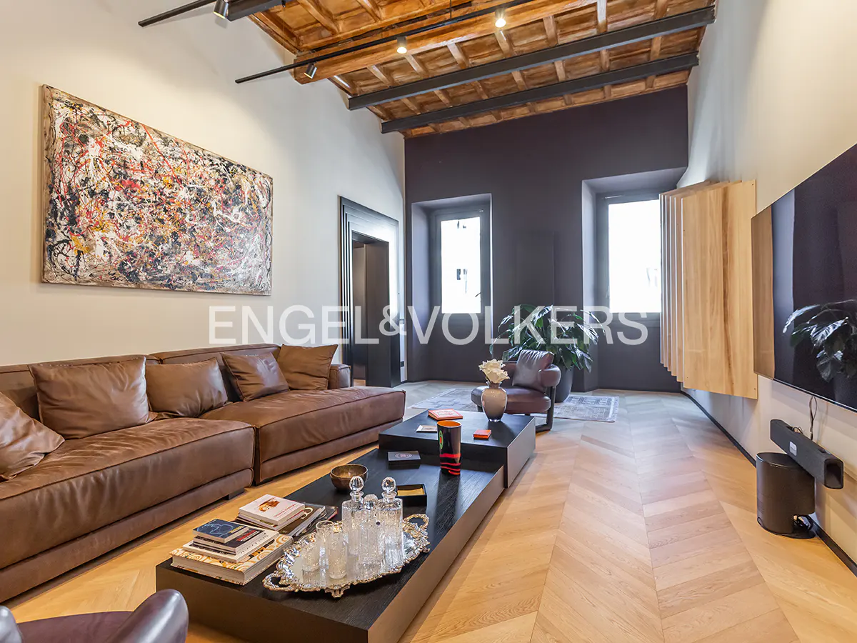 Modern living room with a brown leather sofa, black coffee table, herringbone wood floors, and a large abstract painting.