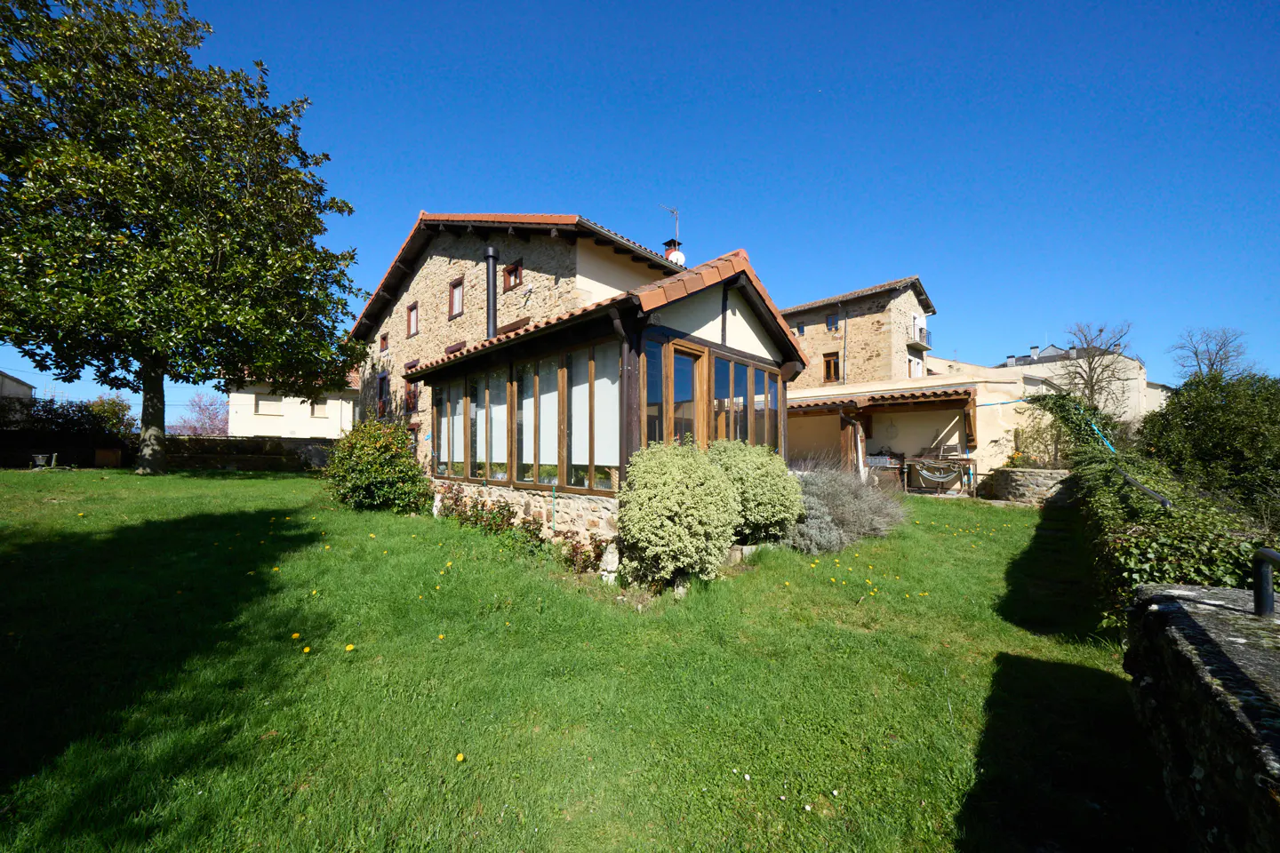 Exterior view of a stone house with a sunroom addition, green lawn, and blue sky.