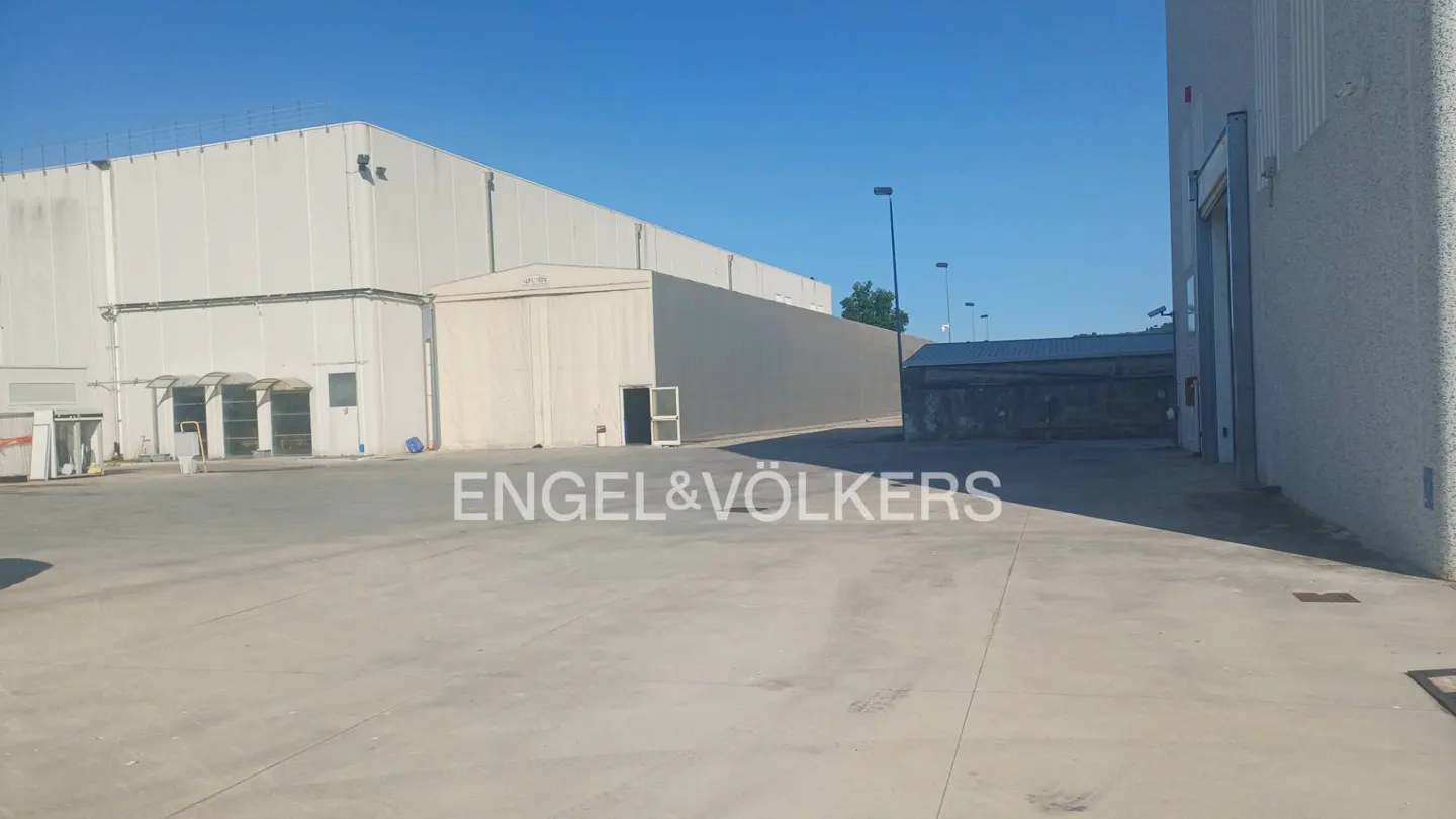 Large industrial warehouse complex with a paved courtyard under a clear blue sky.