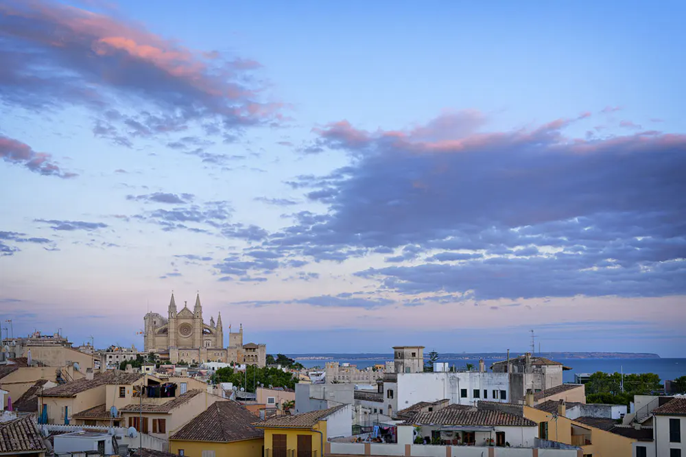 Cityscape view of Palma de Mallorca, Spain, featuring the Palma Cathedral under a blue sky with pink-tinged clouds.