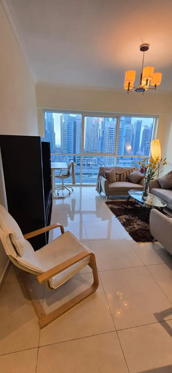A bright apartment living room with a white lounge chair, sofas, and a city view through large windows.