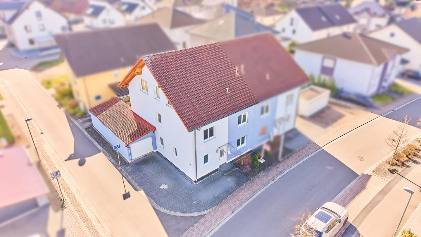 Aerial view of a two-story house with a red tile roof and light blue and white siding, plus a matching detached garage.