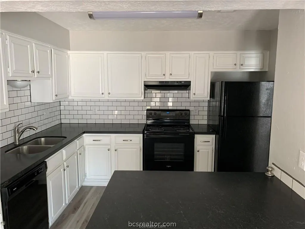 Bright kitchen with white cabinets, black countertops, and subway tile backsplash. Black appliances include a dishwasher, oven, and refrigerator.