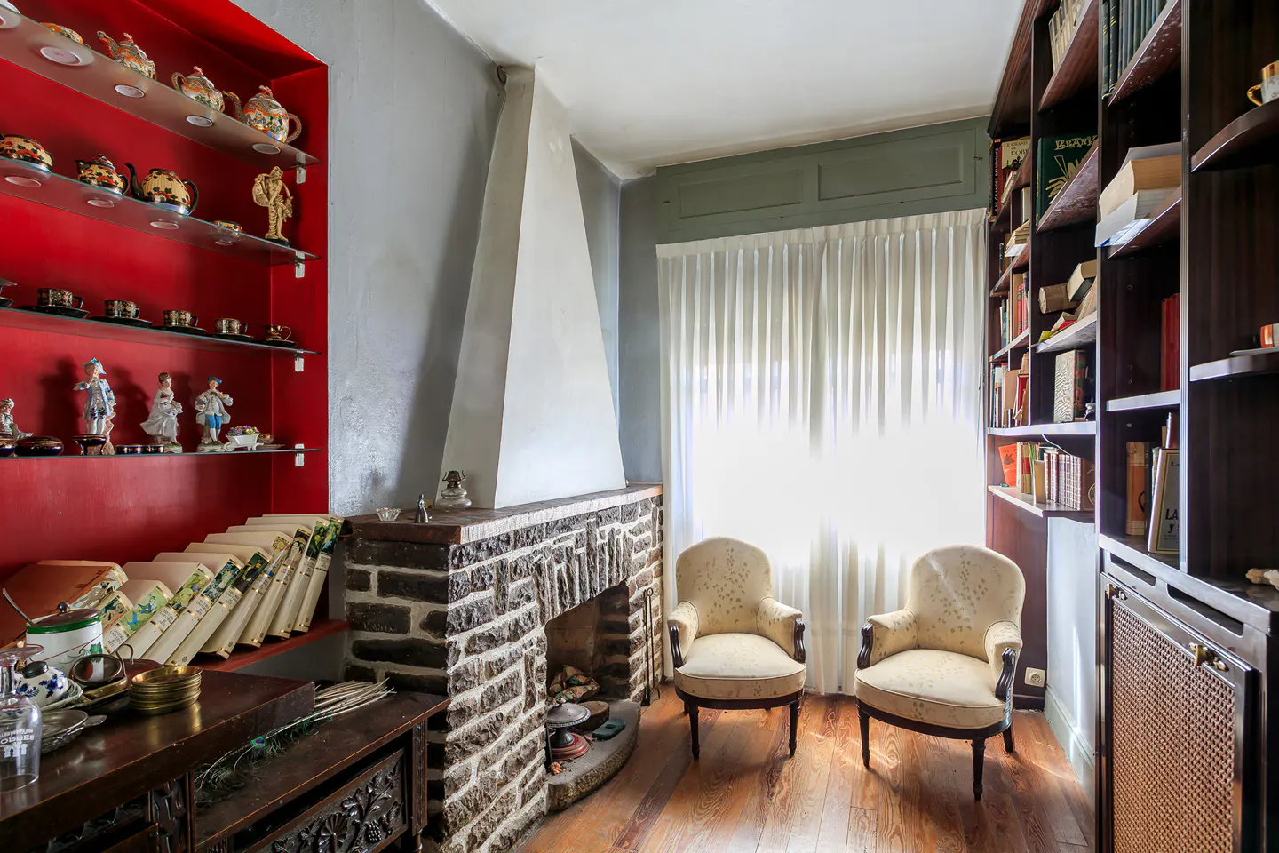 A cozy living room with a stone fireplace, two armchairs, and built-in bookshelves and display shelves.