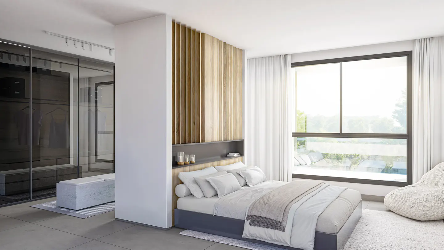 A modern bedroom with a gray bed, white linens, and a wooden headboard. A large window with white curtains lets in natural light. A walk-in closet is visible.