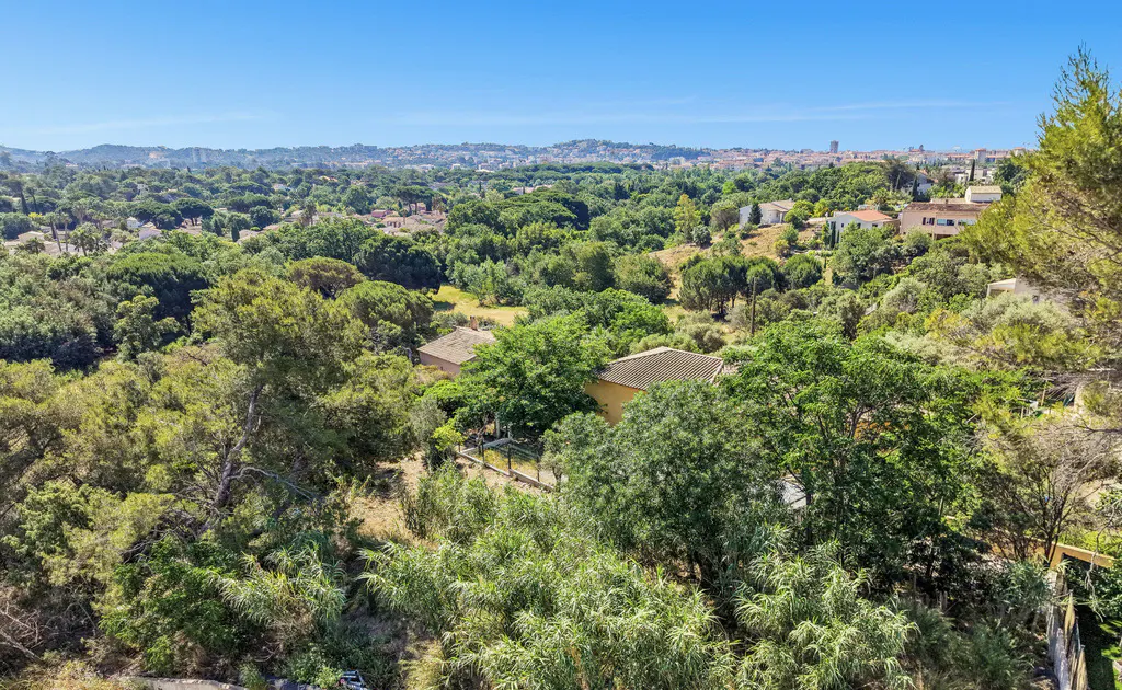 High-angle view of houses nestled in a lush green forest landscape under a clear blue sky.