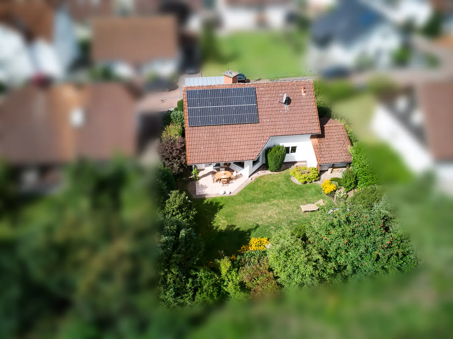 Aerial view of a house with solar panels, a red tile roof, and a green lawn with trees.