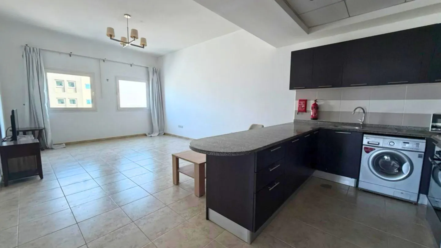 A bright apartment interior with a kitchen, living area, and two windows with curtains.