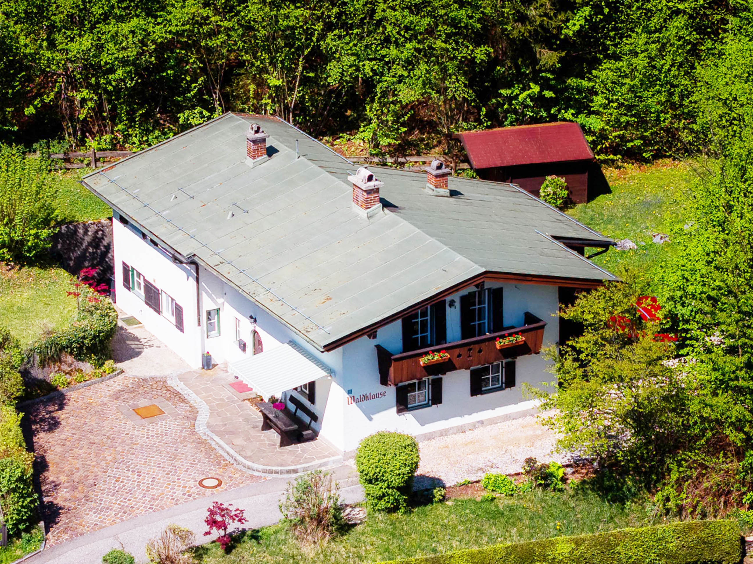 Aerial view of a white house with a gray roof, surrounded by green trees and a red shed.