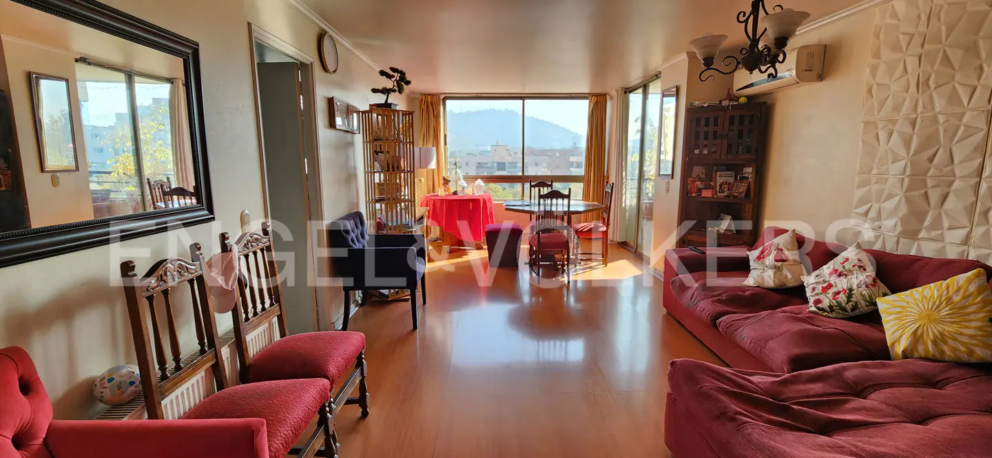 Bright living room with hardwood floors, red sofa, dining table, and large window with a mountain view.