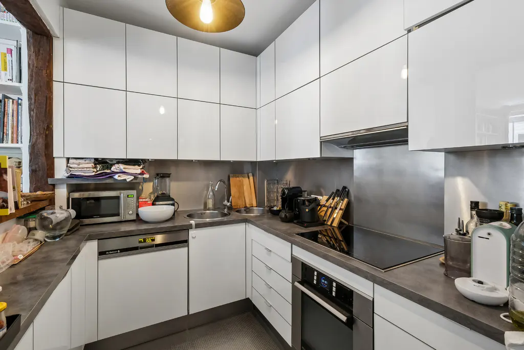 A modern kitchen with white cabinets, gray countertops, and stainless steel backsplash. Appliances include a microwave, dishwasher, oven, and cooktop.