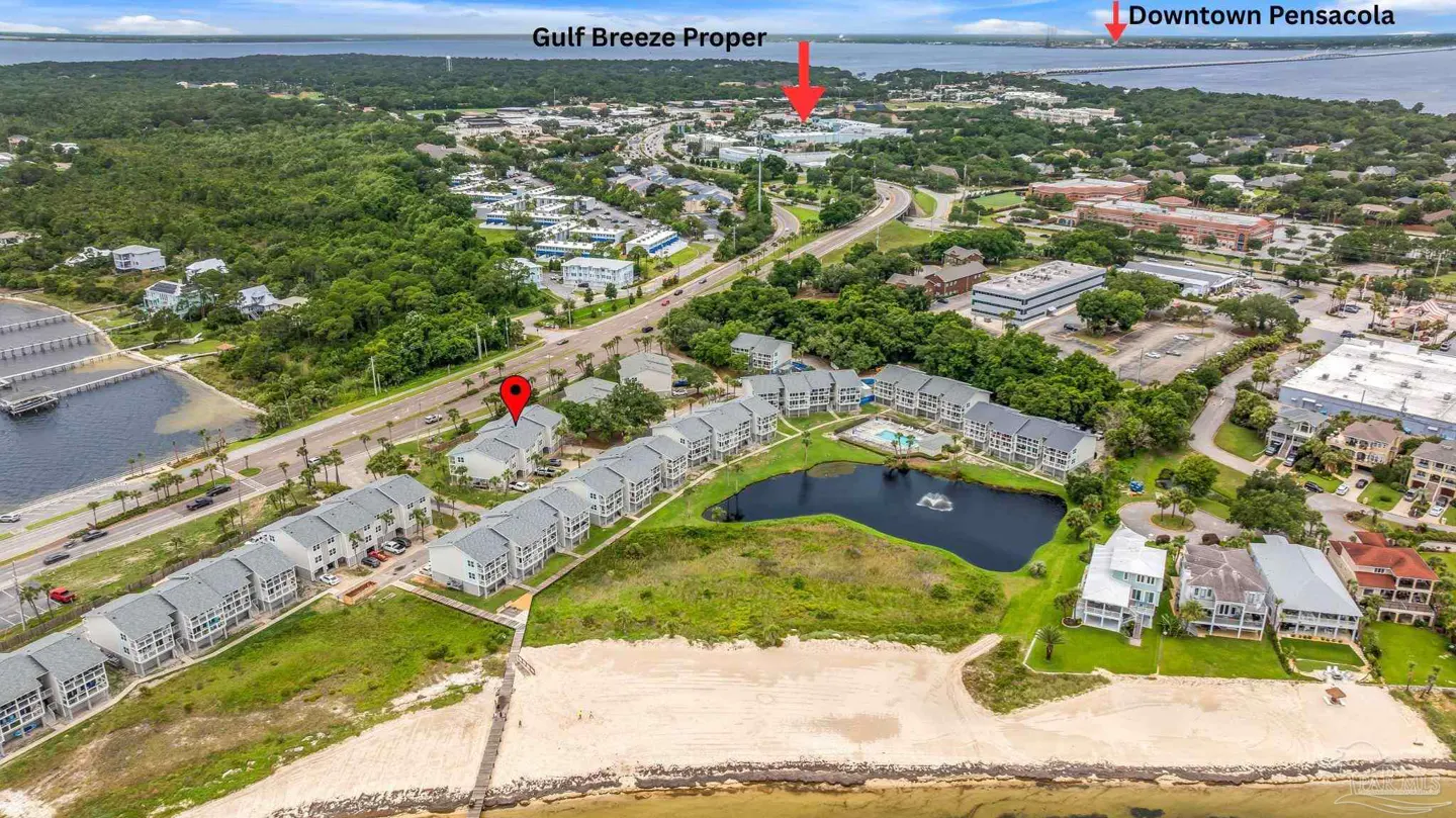 Aerial view of a coastal condo complex with a pond, beach, and red location markers pointing to Gulf Breeze and Pensacola.
