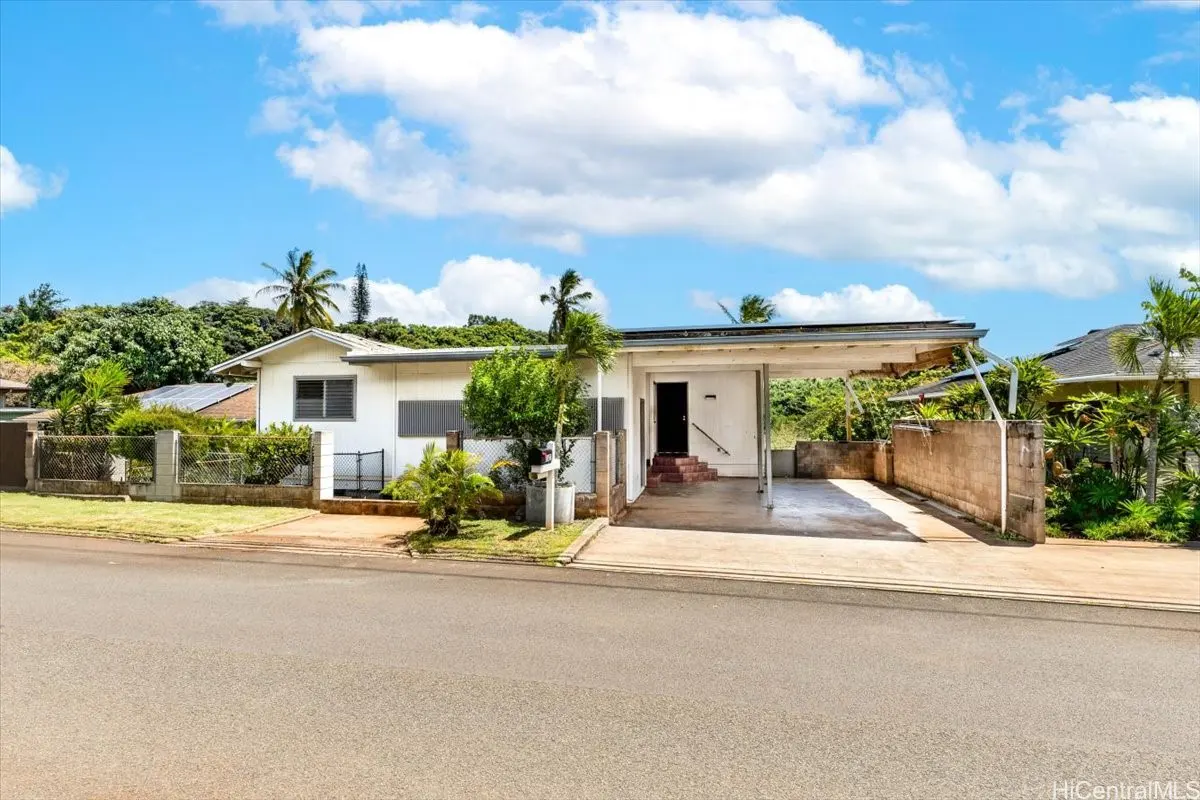 A white single-story house with a carport, green trees, and a blue sky with white clouds.