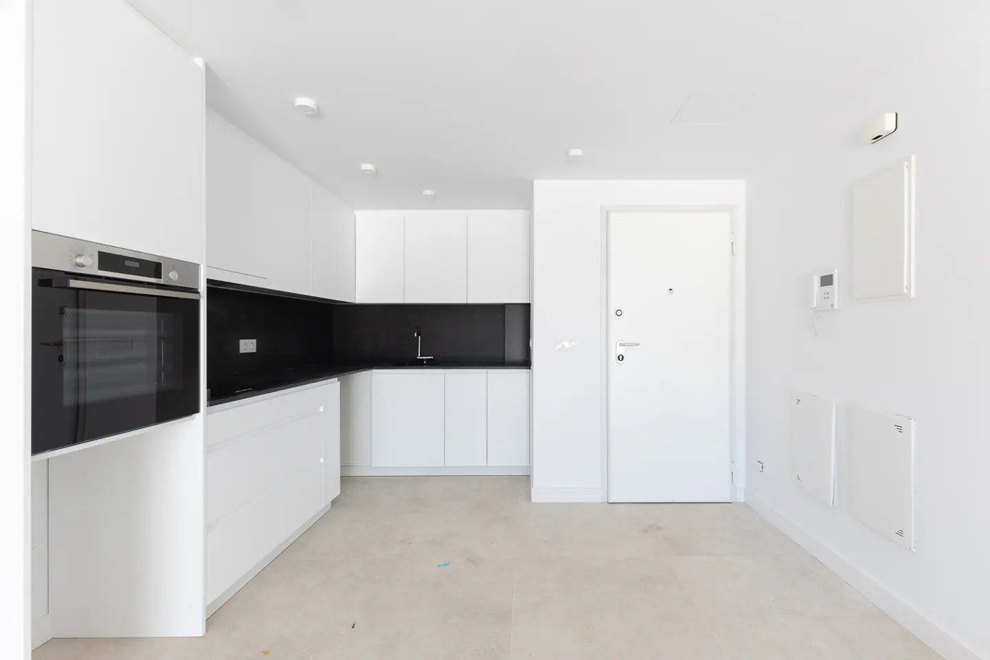 Modern minimalist kitchen with white cabinets, black backsplash, built-in oven, and a white door in a bright, open space.