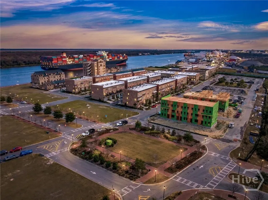 Aerial view of brick townhouses near a river with a cargo ship at sunset. New construction is visible.
