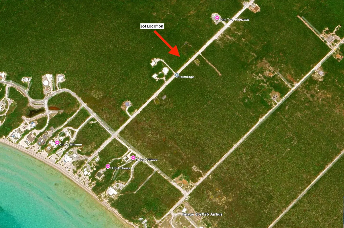 Aerial view of a real estate lot location, indicated by a red arrow, surrounded by green vegetation and roads.