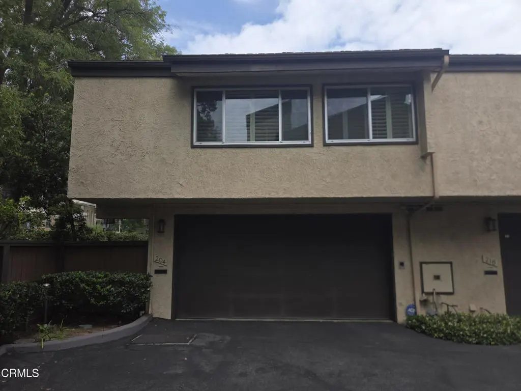 Tan two-story townhouse with a dark brown garage door, two windows, and green bushes.