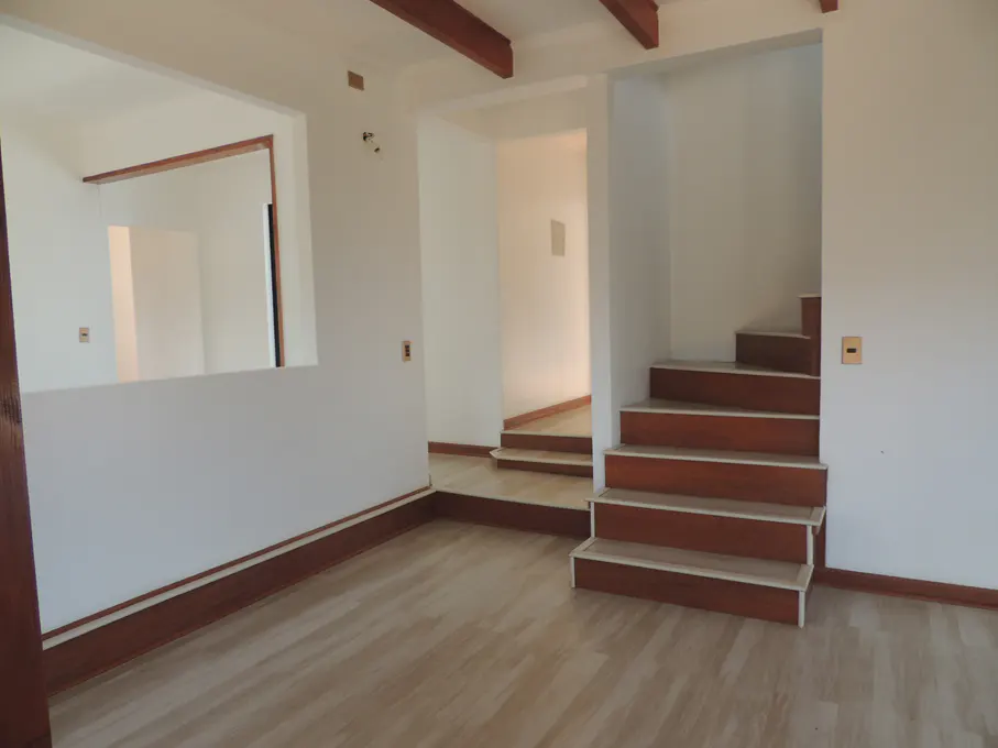 Empty room with light wood floors, white walls, and brown trim. Stairs lead up to a doorway. Beams on the ceiling.