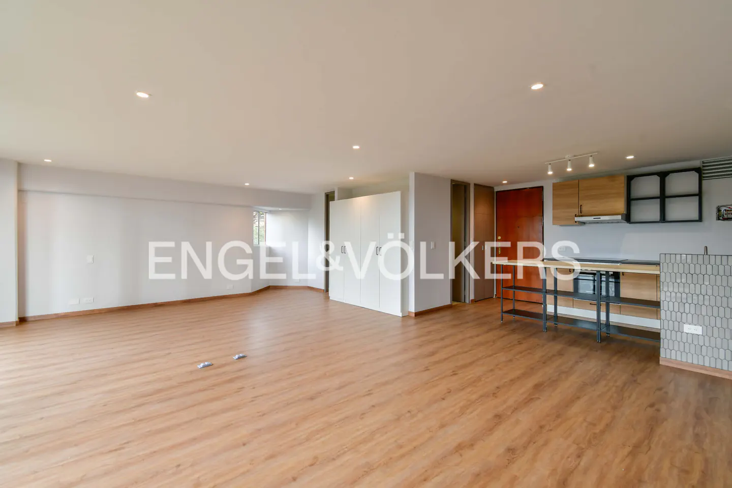 Bright, open-concept apartment with wood floors, white walls, and a modern kitchen area with light wood cabinets.
