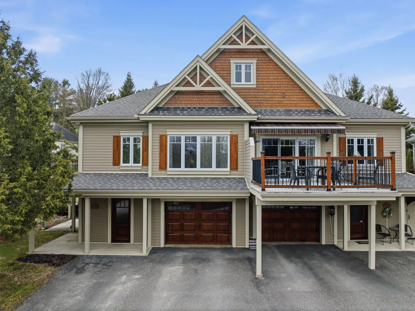Two-story tan townhouse with brown wood accents, a gray roof, and a second-story deck with black railings.
