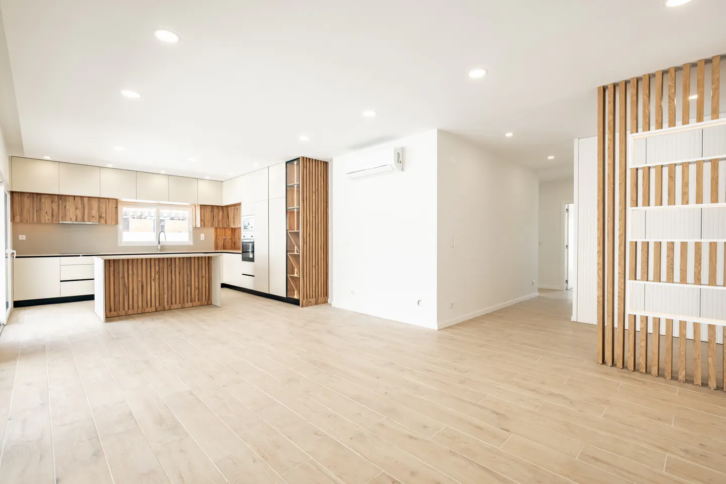 Modern open-plan kitchen with white cabinets, wood-slat accents, a matching island, and light wood flooring.