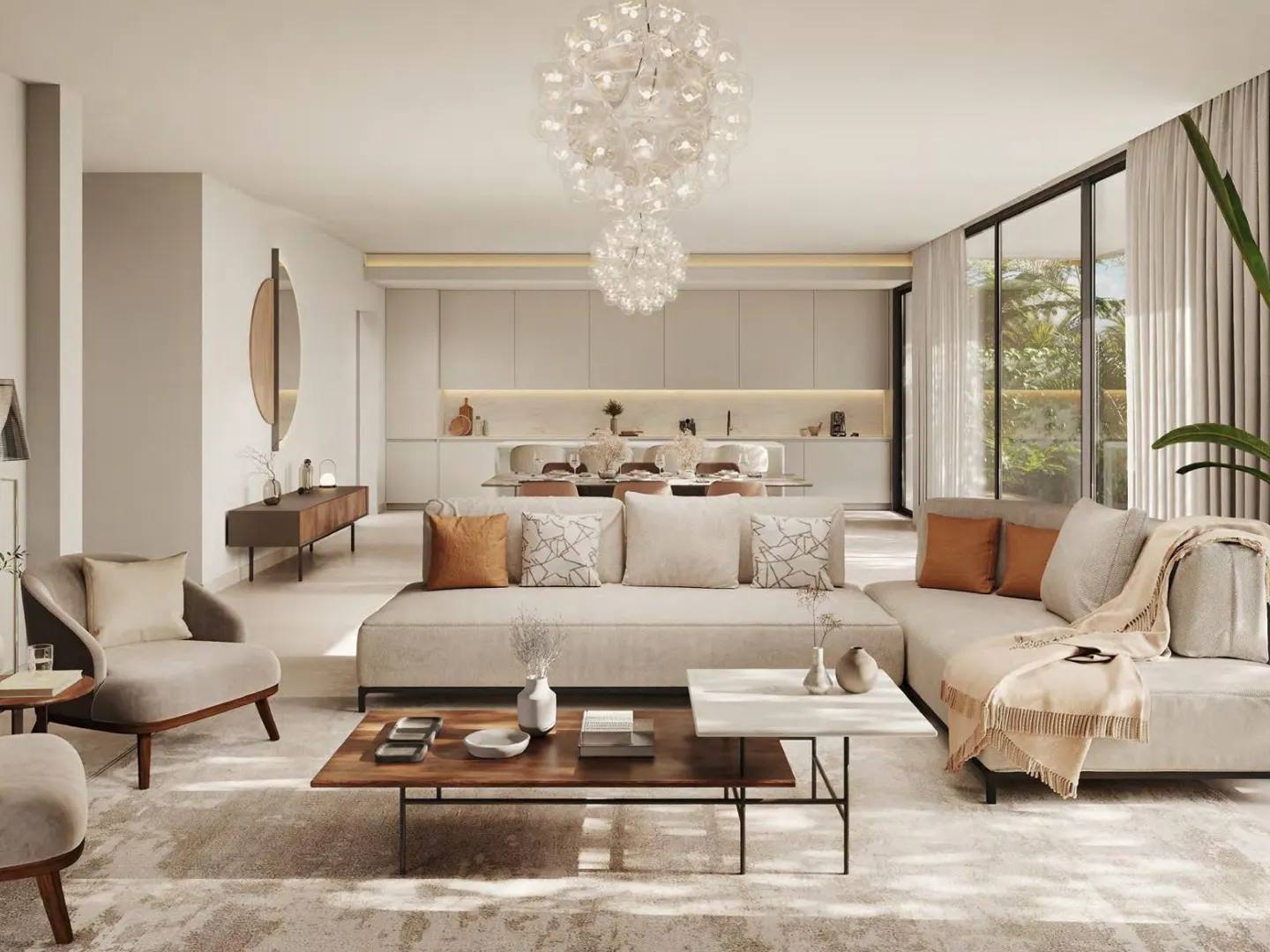 Bright, open-concept living room with beige sofas, wood tables, and a modern chandelier. Kitchen and dining area visible in the background.