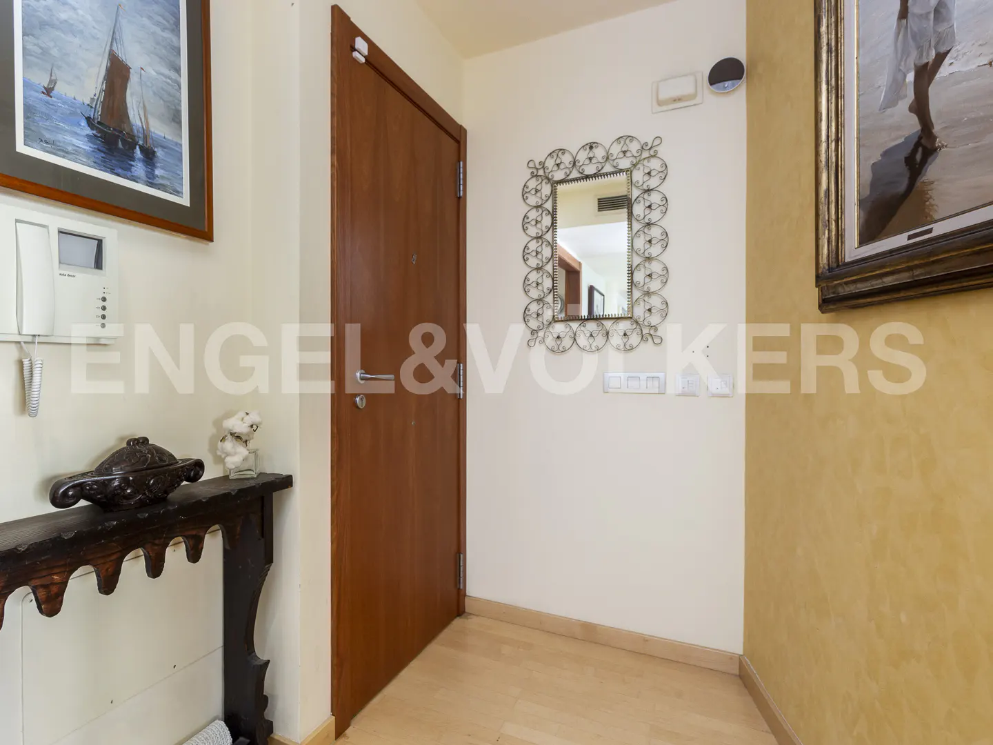 A home's entryway with a wooden door, console table, and decorative mirror. Artwork hangs on the walls.