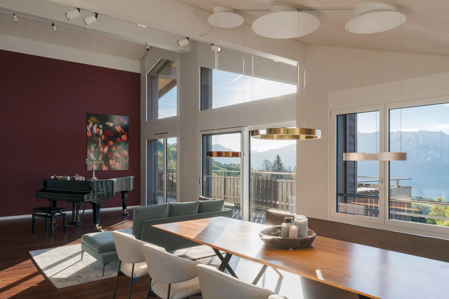 Bright living room with a grand piano, a long wooden table with white chairs, and a view of mountains.