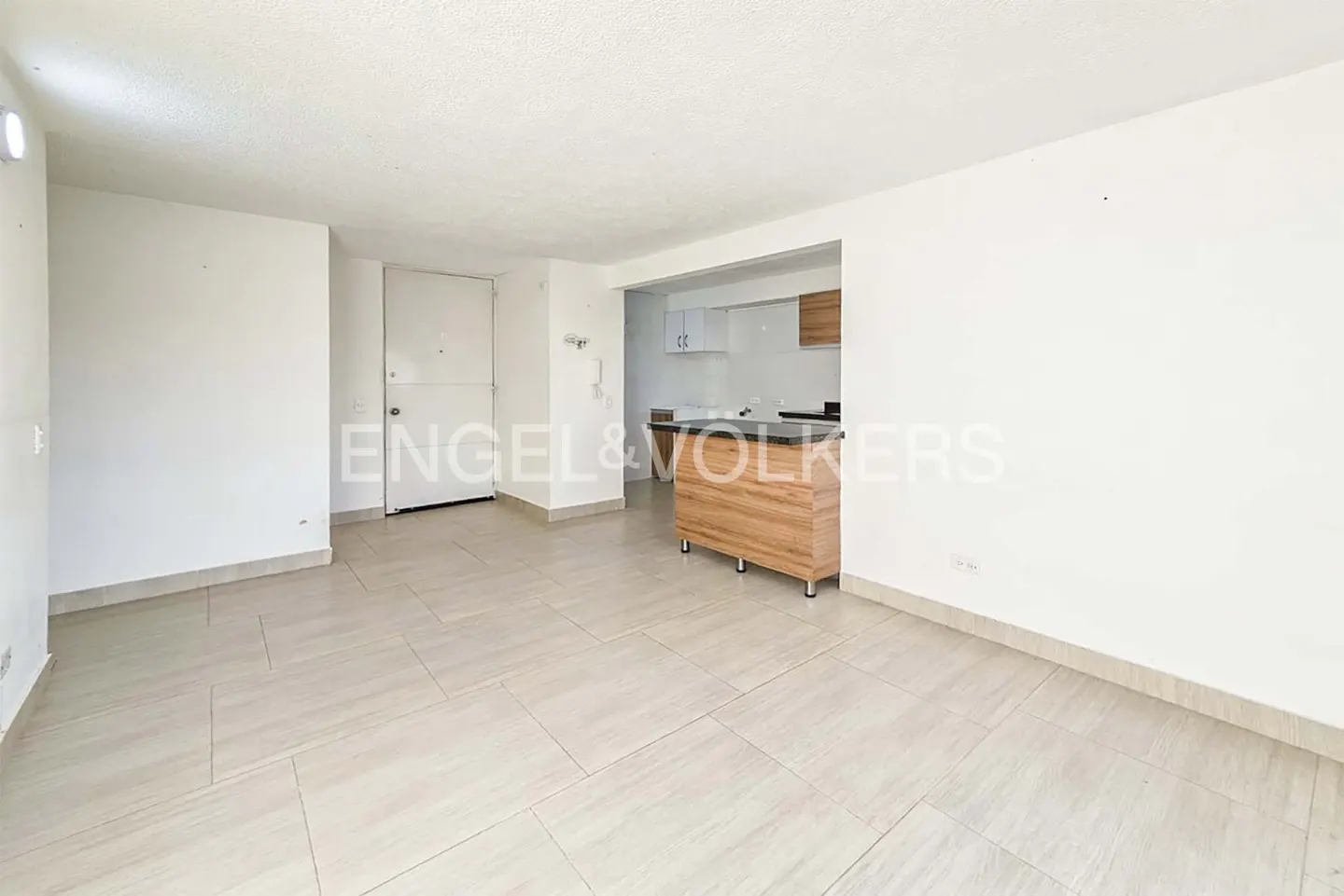Bright, empty apartment with white walls, tile floors, and a wood kitchen island. A white door is on the left.