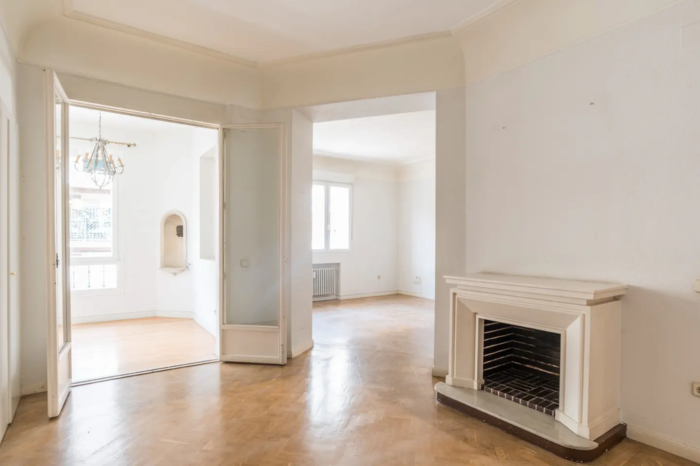 An empty room with white walls, a fireplace, and open doors leading to another room.