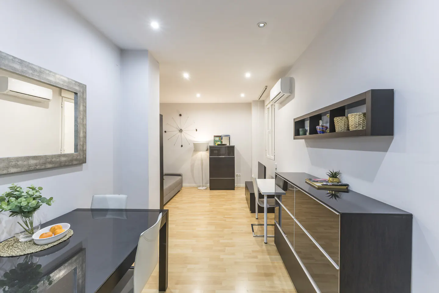 A bright, modern apartment interior with a black dining table, wooden floors, and minimalist decor.