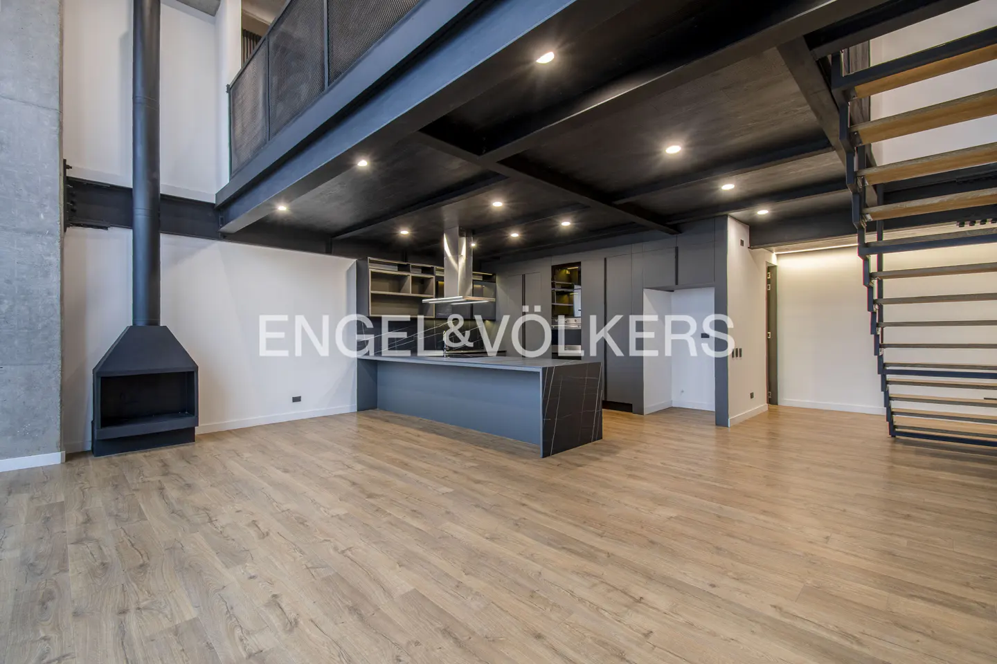 Modern industrial loft with wood floors, a black fireplace, a sleek kitchen island, and an open staircase.