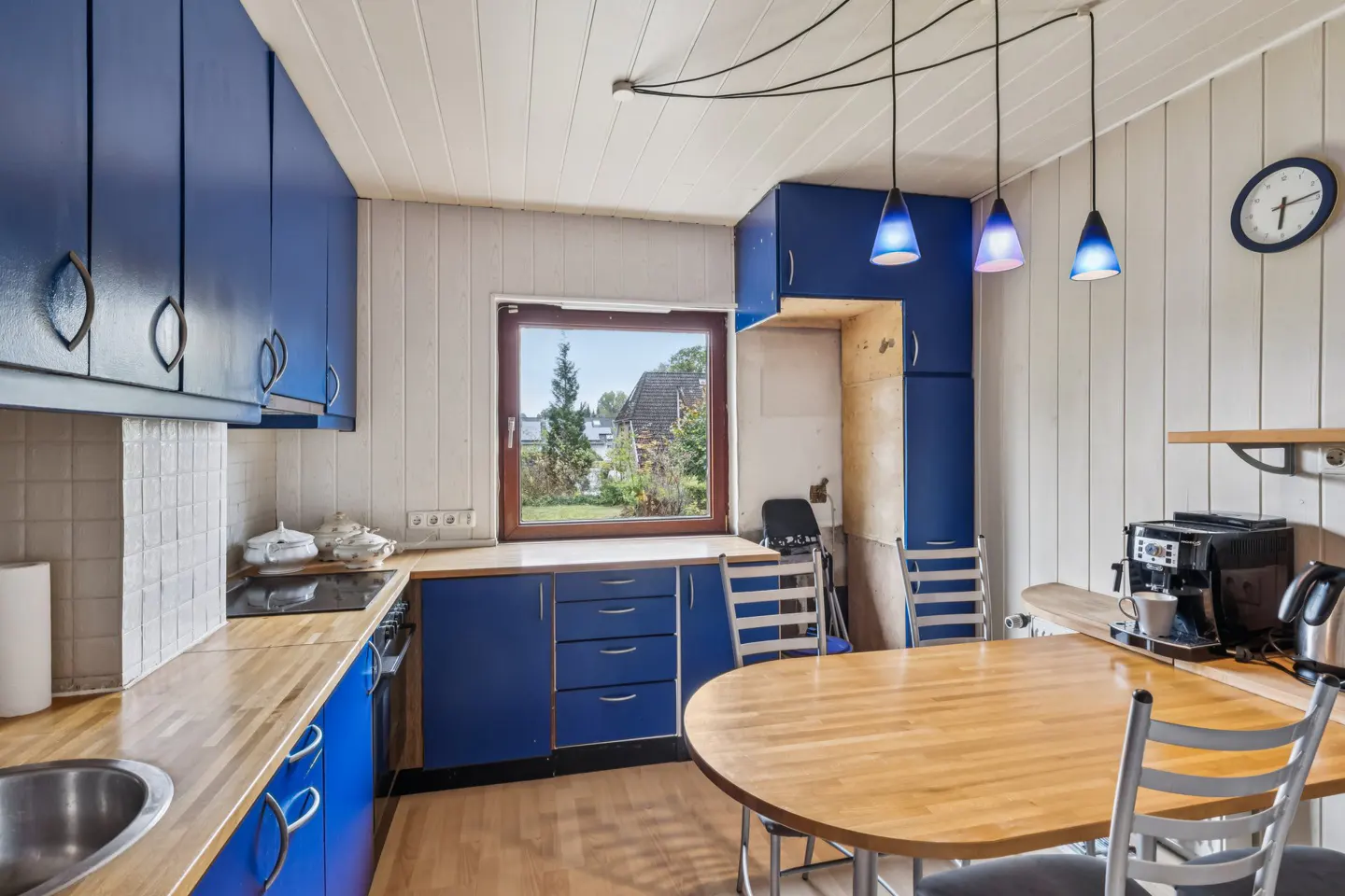 Kitchen with blue cabinets, wood countertops, a round dining table, and a window looking out to a garden.