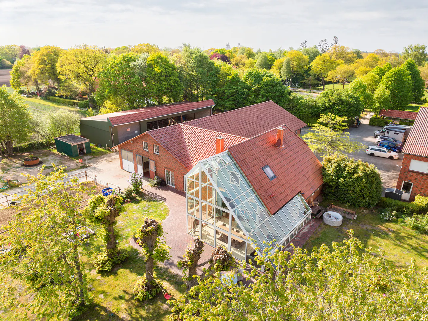 Aerial view of a red brick house with a glass conservatory, surrounded by green trees and a lawn.