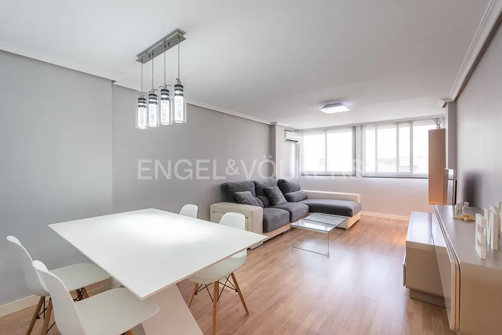 Living room with gray walls, wood floors, white table and chairs, gray sofa, and modern lighting.