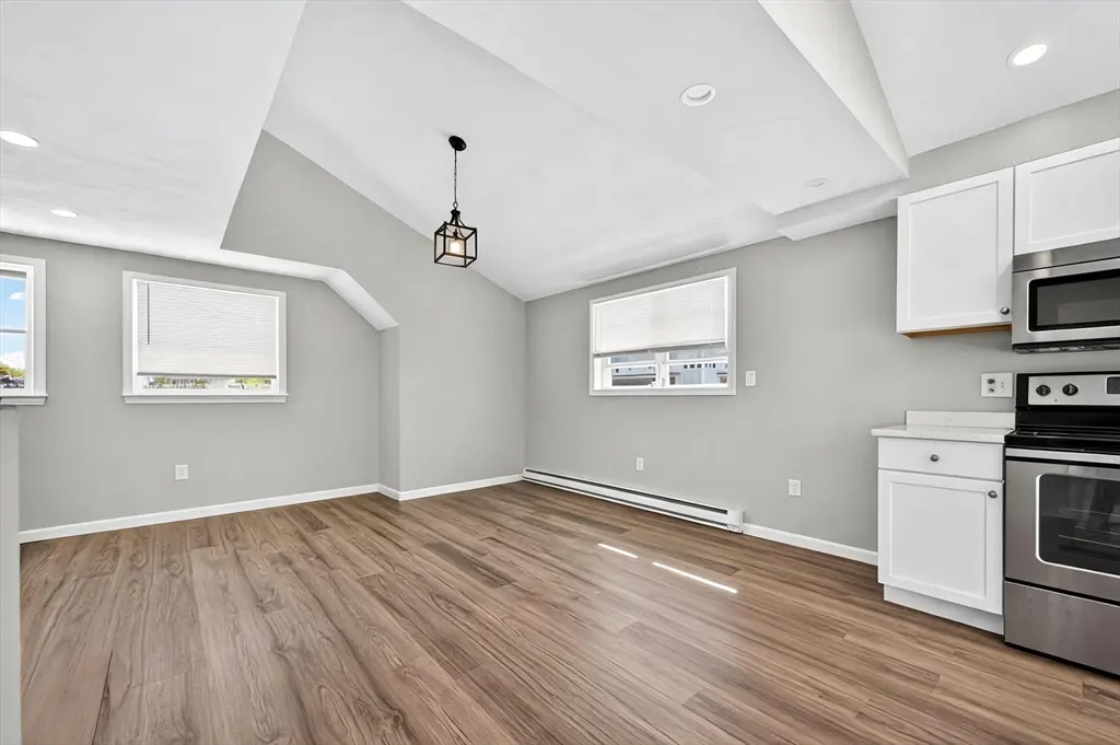 Bright, modern kitchen with wood floors, gray walls, and white cabinets. Stainless steel appliances and a black pendant light add contrast.