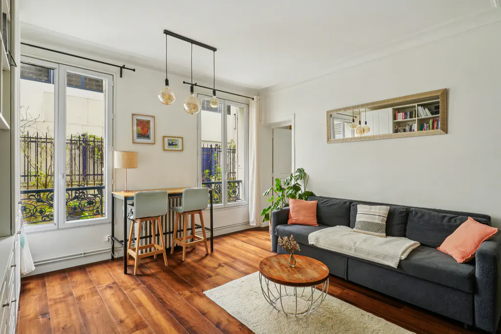 Bright living room with hardwood floors, dark grey sofa, round wooden coffee table, and a breakfast bar by the window.