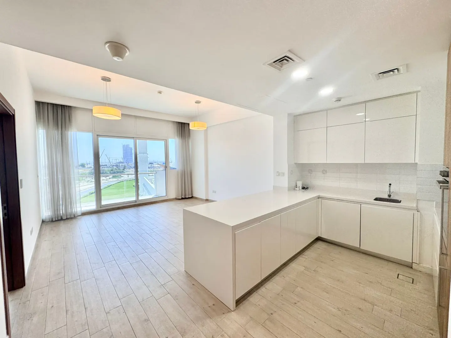 Bright, modern apartment interior with white kitchen island, cabinets, and wood-look flooring. Large windows offer a city view.