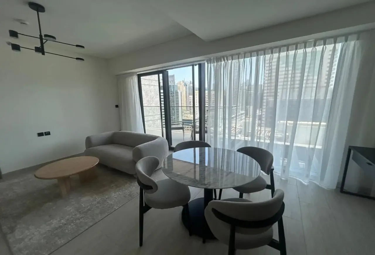 Modern living room with a grey sofa, round marble dining table, four chairs, and floor-to-ceiling windows with city views.