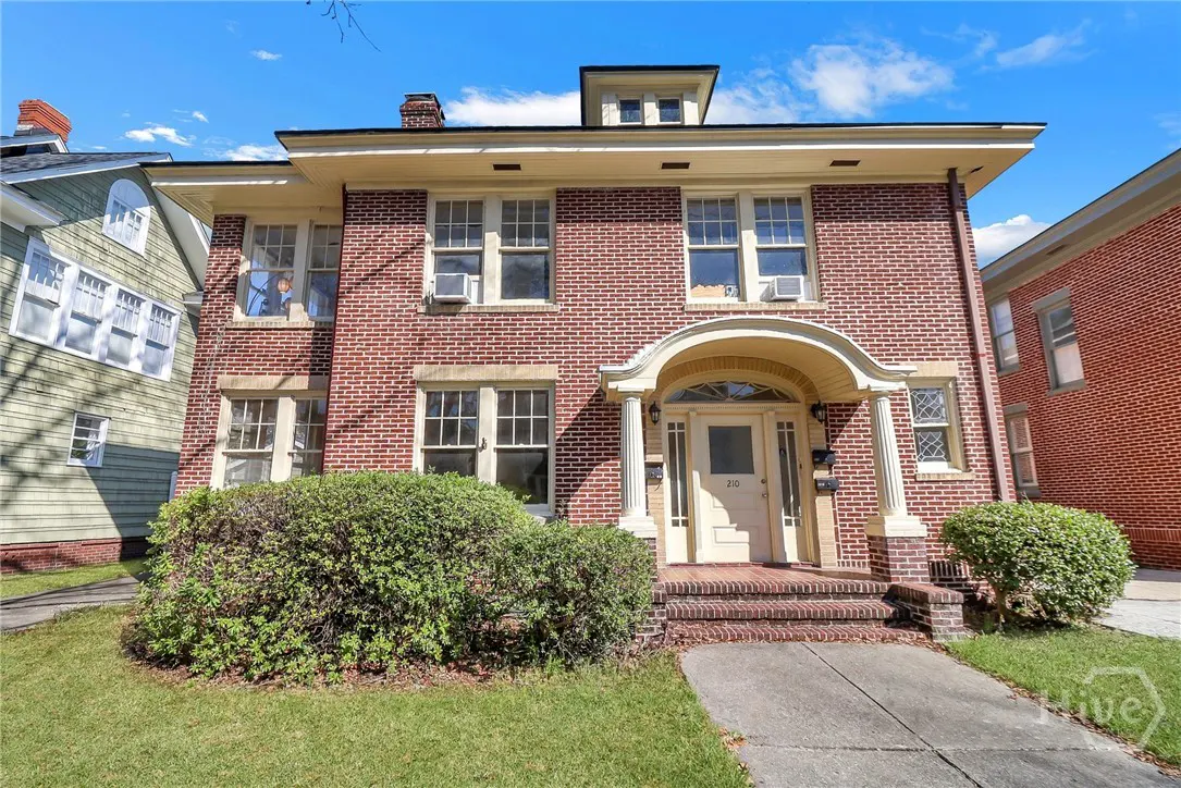 Two-story brick house with white trim, arched porch, and green lawn on a sunny day.