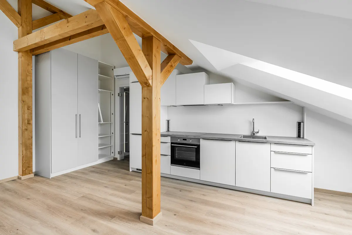 Bright, modern kitchen with white cabinets, grey countertops, and wood floors. Exposed wooden beams add rustic charm to the attic space.