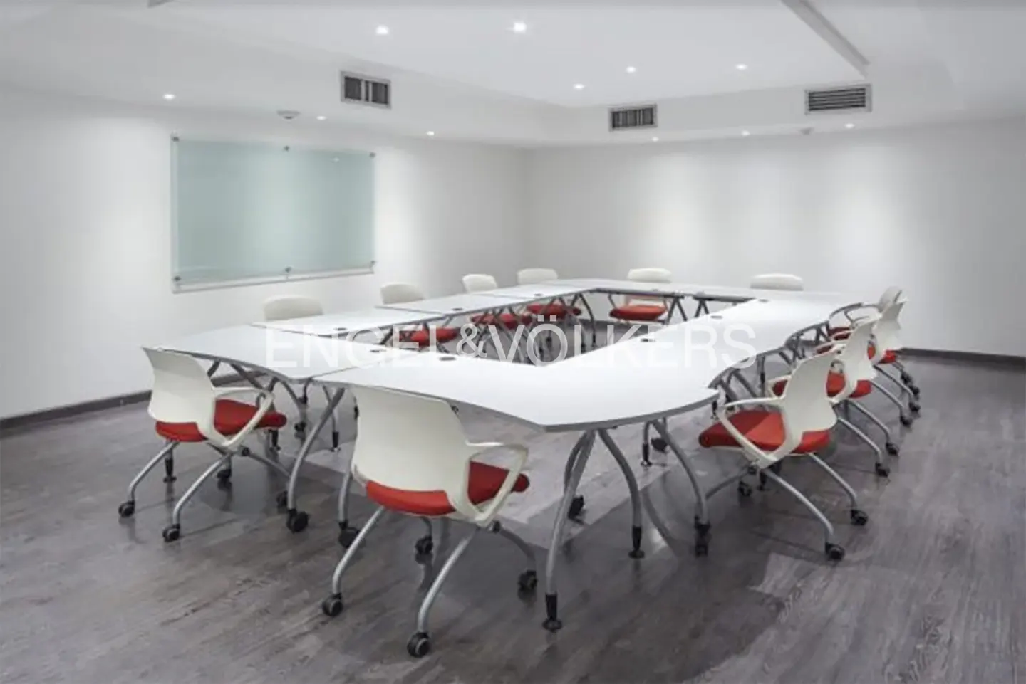 Bright meeting room with a U-shaped table, white chairs with red cushions, and a whiteboard on the wall.