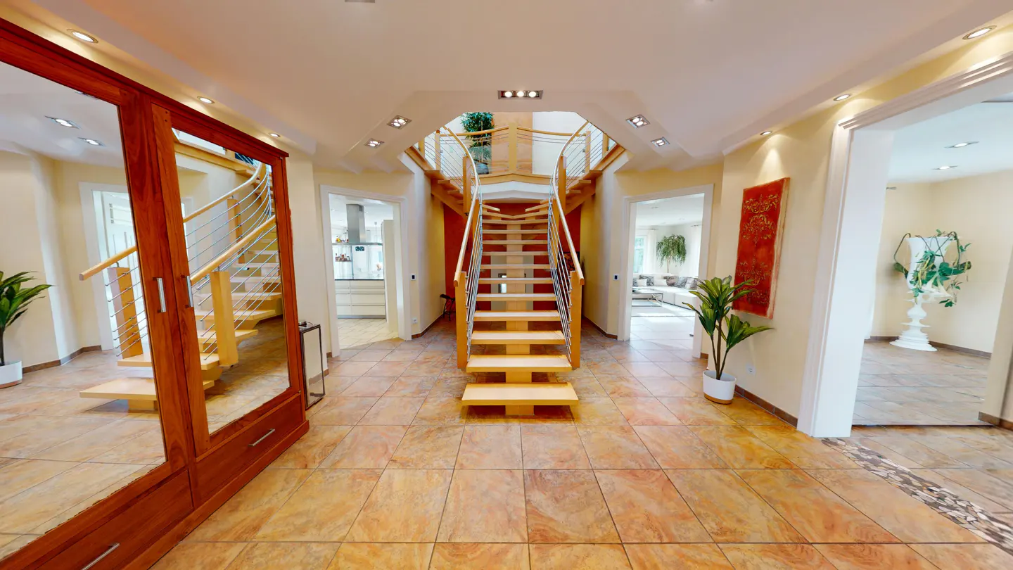 A wide shot of a home's foyer with a wooden staircase, tile floors, and a large wooden cabinet.
