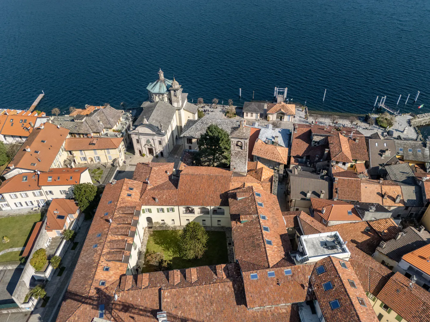 Aerial view of Isola San Giulio, Italy, with terracotta rooftops, a church with a blue dome, and blue lake water in the background.